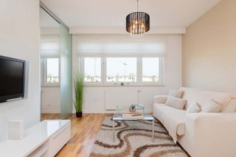  A cozy living room featuring a beige sofa, a small coffee table, and bright natural light from large windows.