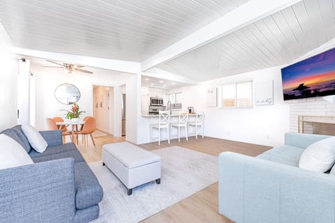 The living area includes a sofa set, streaming TV (Youtube TV), dining for four, and bar seating, all with a white, clean, beachy motif.
                