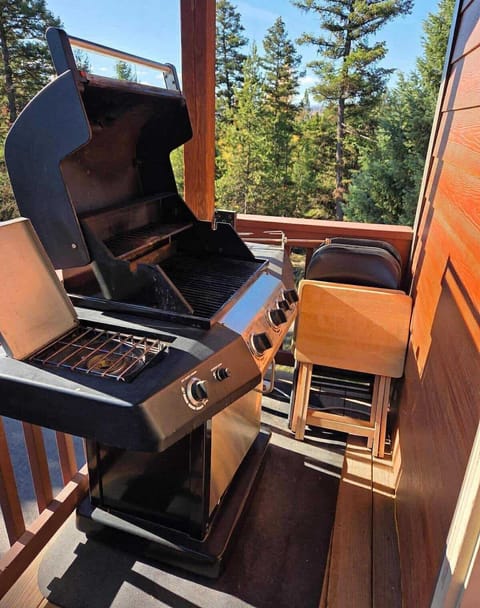 Gas BBQ grill with rotisserie on the balcony with chairs and trays.