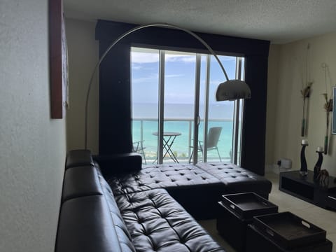 Ocean view Living room w/Flat smart TV, sofa bed, and blackout shades.