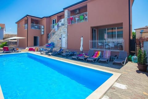 The outside of the house and the swimming pool area equipped with deck chairs and umbrellas