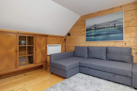 A spacious bedroom which has been furnished with a grey sofa bed and a wooden chest of drawers. Above the sofa is a large painting with a panorama of the city.