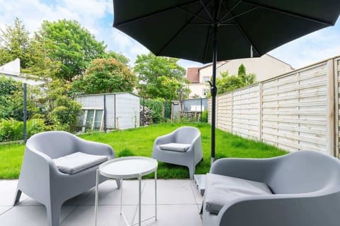 Outdoor seating area with gray furniture and umbrella, next to a small lawn.