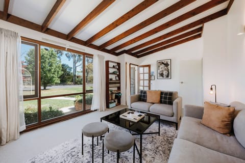 A light-filled, cosy living area invites relaxation, with soft grey lounges, a large-screen TV, and tranquil leafy views.