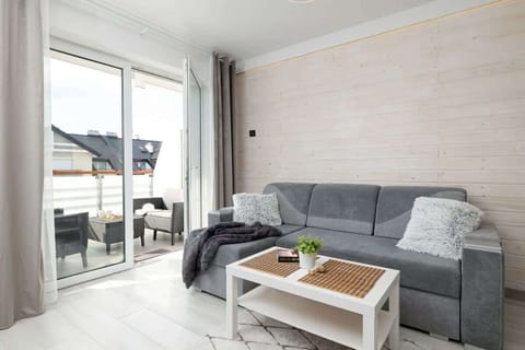 A cozy living room with a light gray corner sofa, a coffee table, and a modern decor theme in soft tones, complemented by a large window for natural light.