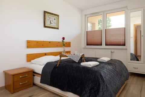 A cozy bedroom with a comfortable double bed, gray bedding, wooden headboard, and bedside table featuring a flower vase.