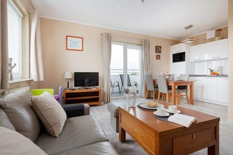 The living room from a different perspective, featuring a large window letting in natural light and a TV on a wooden stand.