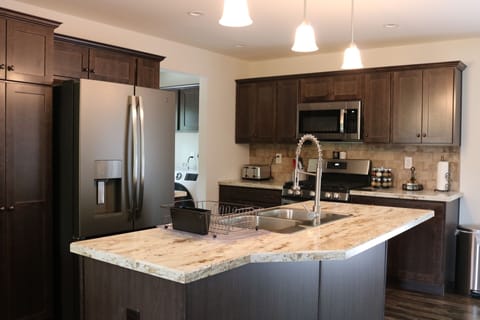 Kitchen has a fridge, stove, dishwasher. Laundry room in the background. 