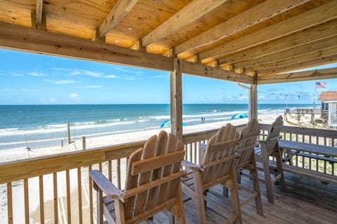 Covered oceanfront deck with Adirondack chairs overlooking the beach and waves—perfect for relaxing, dining, and enjoying stunning Oak Island, NC coastal views.