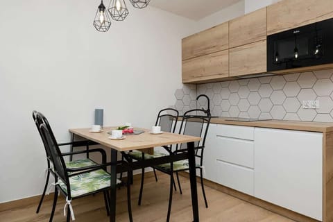 A view of the kitchen and dining area. The kitchen is modern with white cabinets and wooden accents, and the dining table has a simple, functional design with black chairs.