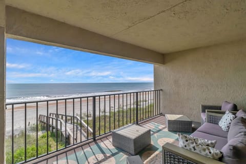 - Soak in endless ocean views from this covered balcony with cozy lounge seating
- Area rug, outdoor pillows, and wicker furniture create the ultimate beachside retreat
- Stairs lead directly down to the sandy shoreline just steps away