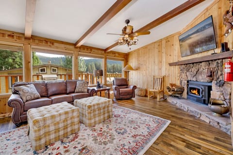 Cozy mountain living room with a stone fireplace, comfy seating, and smart TV—perfect for relaxing evenings, movie nights, and warm cabin vibes after outdoor adventures.