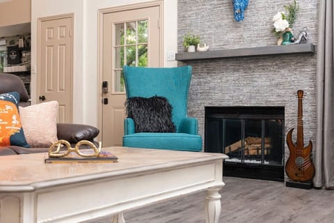 Sink into a bold teal accent chair beside the stone fireplace, where layered textures create a cozy, design-forward retreat.