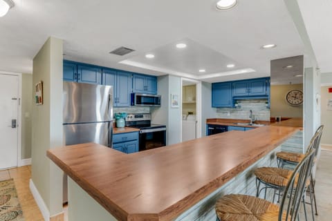 Cook with ease in the fully equipped kitchen featuring sleek stainless steel appliances and a vibrant pop of blue for a coastal touch