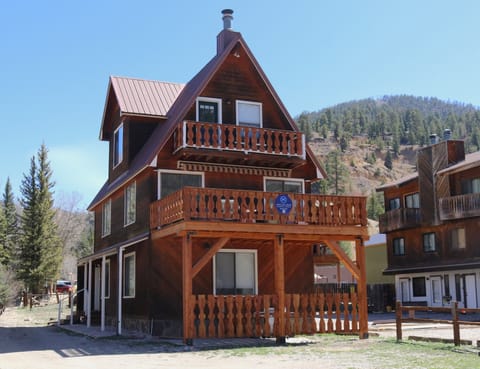 A charming three-story alpine chalet nestled in a forested mountain valley, offering a secluded retreat surrounded by natural beauty and neighboring homes.