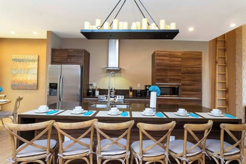 Warm, modern kitchen with rich wood cabinetry, stainless appliances, and a long island with ample seating beneath a candle-style chandelier-ideal for cooking together and casual breakfasts.