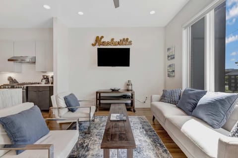 Cozy living room with a cream sofa, matching chairs, a warm wooden coffee table, and soft denim-toned accents—natural light pours in through large windows with scenic views.