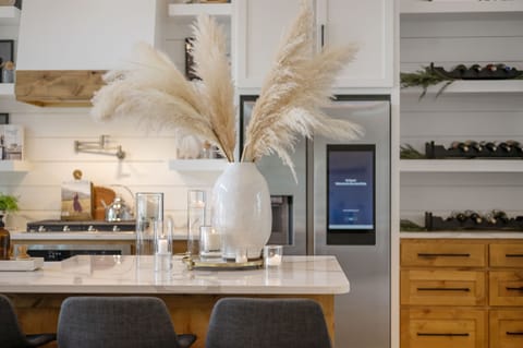 This elegant kitchen features sleek white cabinetry, natural wood accents, and modern decor, creating a warm and inviting space for cooking, gathering, and entertaining guests.