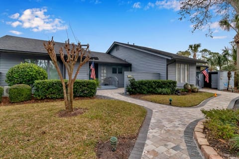Charming entryway with curved paver path, manicured hedges, and coastal gray exterior.