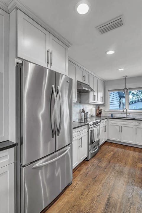 - Modern stainless steel French door fridge anchors this bright kitchen with sleek cabinetry and subway tile backsplash
- Built in microwave, electric range, and full size oven ready for group meals
- Warm wood floors and natural light make cooking a joy