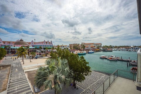 A stunning marina scene with colorful Dutch Colonial architecture, palm trees, and boats docked in turquoise waters under a dramatic cloudy sky.