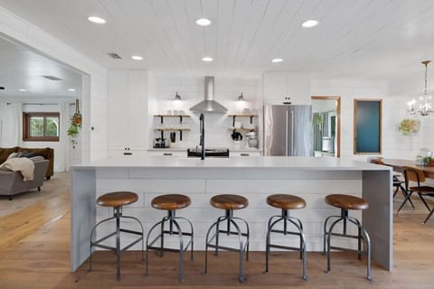 Bright farmhouse kitchen with open shelving and river‑view dining table—cook together, then step right out to the treetop deck.