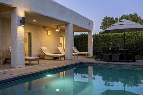Multiple lounge chairs and an outdoor dining table with umbrella, arranged along the covered patio beside the pool.