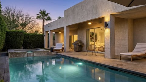 A covered patio with lounge seating and a built-in BBQ, positioned right off the main living space and overlooking the pool.