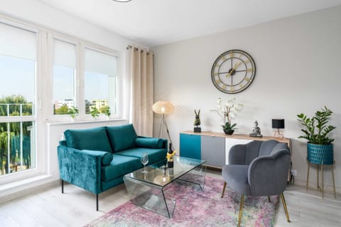 A bright living room with a teal sofa, a cozy armchair, and large windows that fill the space with natural light.