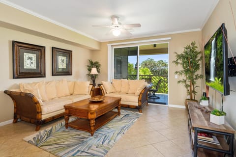 - Spacious living room with tile floors, neutral tones, and tropical style seating for relaxation - Sliding doors open to a breezy lanai with beautiful green views just beyond - Ceiling fan and soft lighting create a comfortable, airy retreat