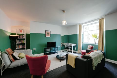 The stylish living room features a smart TV, sofa bed, and a workspace desk