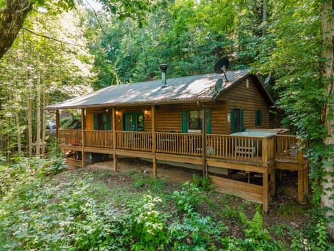 A full view of the log cabin surrounded by mature trees highlights the peaceful forest setting in Bryson City, NC. This secluded Smoky Mountain retreat offers a spacious covered deck for relaxing outdoors.