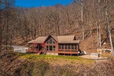 Exterior view of Millstone Lodge surrounded by wooded mountain landscape in Bryson City, North Carolina. The single-level cabin features a covered deck and peaceful Smoky Mountain setting.