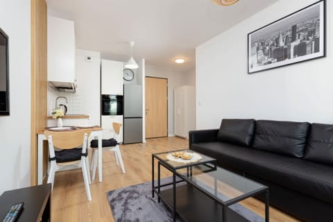 A bright and spacious living room with a sofa, coffee table, and a view of the modern, open kitchen.