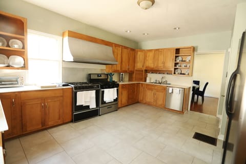 Kitchen shown with portion of the Dining Room in the background. The Kitchen includes a sink and a dishwasher adjacent to the Dining Room, the stoves and cooking surface to the left and the fridge to the right.