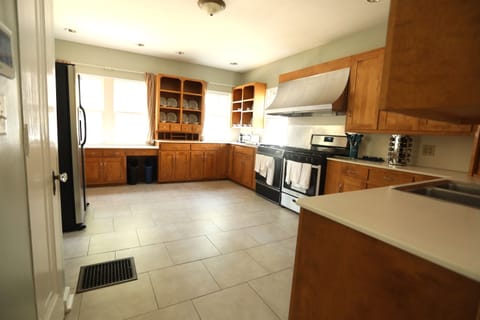 Kitchen shown with back to the Dining Room. The ADT panel and pantry are on the left. Four windows bathe the Kitchen in natural light arrested only by three sheer curtains and a set of blinds.