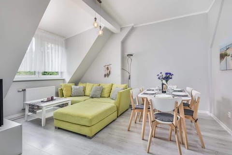 A modern and bright living room space with a large yellow sofa that stands out against the grey walls. Next to the sofa is a large dining table.