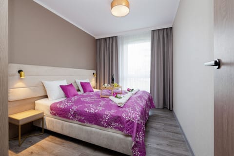 A cozy bedroom featuring a large bed with purple bedding, bedside tables, and a warm, neutral wall color.