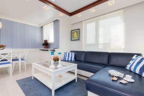 A bright living room with blue and white striped decor, including a navy sofa and a white coffee table. Large windows provide ample natural light.