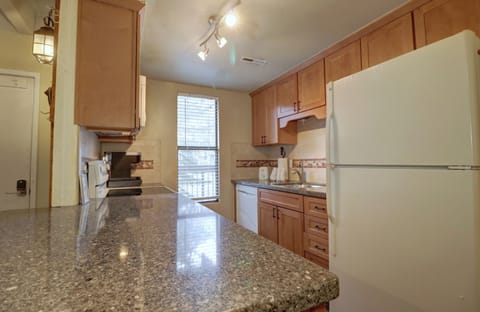 A kitchen with wooden cabinets, a granite countertop, a white refrigerator, and a white dishwasher. A window allows natural light to enter the space.