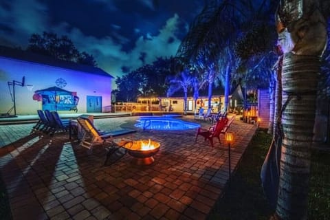 A serene backyard at night, illuminated by the soft glow of a fireplace. The sparkling pool reflects the starry sky, creating a perfect oasis for relaxation and evening gatherings under the moonlight.
