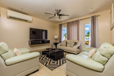 A living room filled with a comfortable sofa. There is an air conditioning unit and ceiling fan. There's a TV for entertainment and large curtains for privacy
