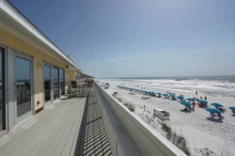 Beachfront property featuring a spacious deck overlooking pristine white sand beach with turquoise umbrellas and gentle surf.