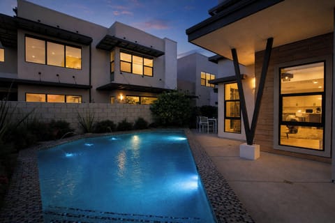 Modern architectural masterpiece featuring a pristine swimming pool illuminated at twilight, surrounded by contemporary design and warm interior lighting throughout multiple levels.
