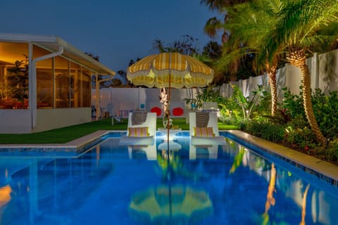Private pool lit up at night with palms, ambient lighting, and a relaxed retro-coastal vibe.