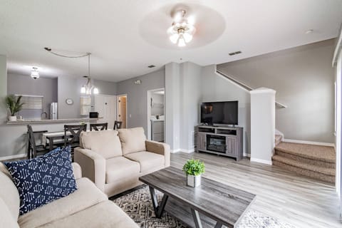 The cozy living area features a plush beige sofa paired with a textured navy pillow, inviting you to unwind. Natural light floods in, enhancing the open layout that seamlessly connects to the kitchen, perfect for socializing.