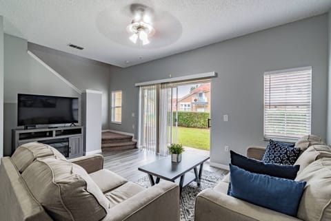 This bright, airy living room boasts cozy beige sofas with deep blue pillows, inviting relaxation. Large sliding doors reveal a lush outdoor view, filling the space with natural light and fresh air for your enjoyment.