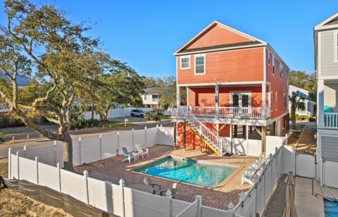 Charming coral beach house with private pool surrounded by white fencing in a peaceful residential neighborhood.