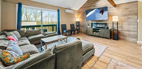 Living room featuring a 75 inch smart TV with Netflix and Roku. Connects to Balcony with mountain view blue sky and trees. Board games for family, comfortable couch, ample lighting.