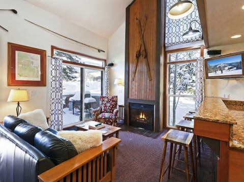 A leather couch, cozy armchair, striking wood-paneled fireplace, flat-screen TV and large windows highlighting this home’s terrific location with ski in/ski out access to Park City make for an inviting living space.